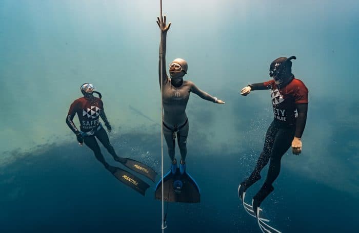 A freediver competing in a freediving competition ascending with safety divers in tow.