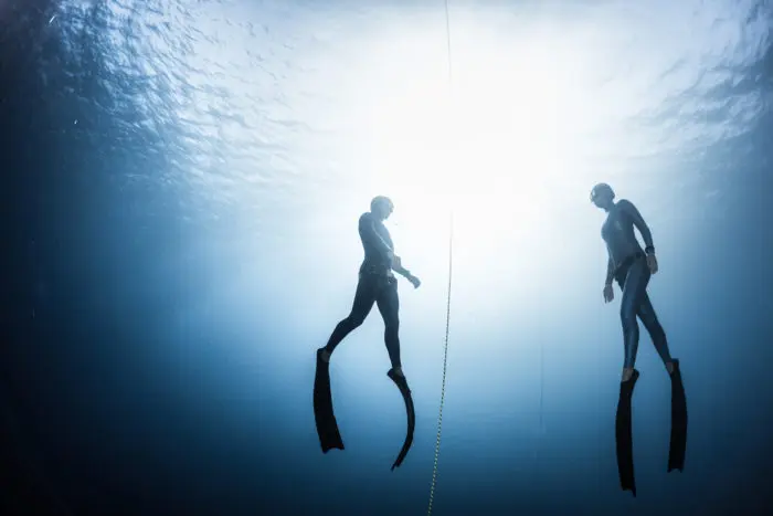 A freediving instructor ascending with a student.