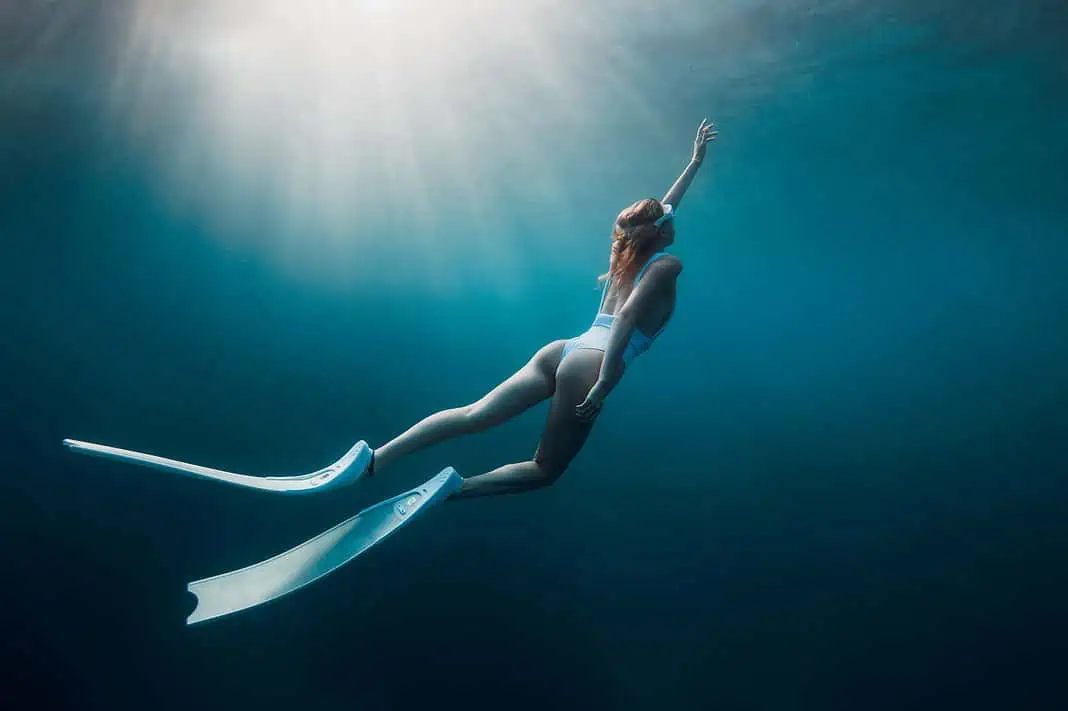 Woman freediver with white fins underwater. Freediving with beautiful sun rays in the Ocean