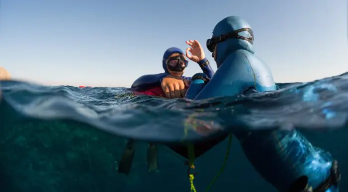 Split shot of two free divers training in sea with buoy